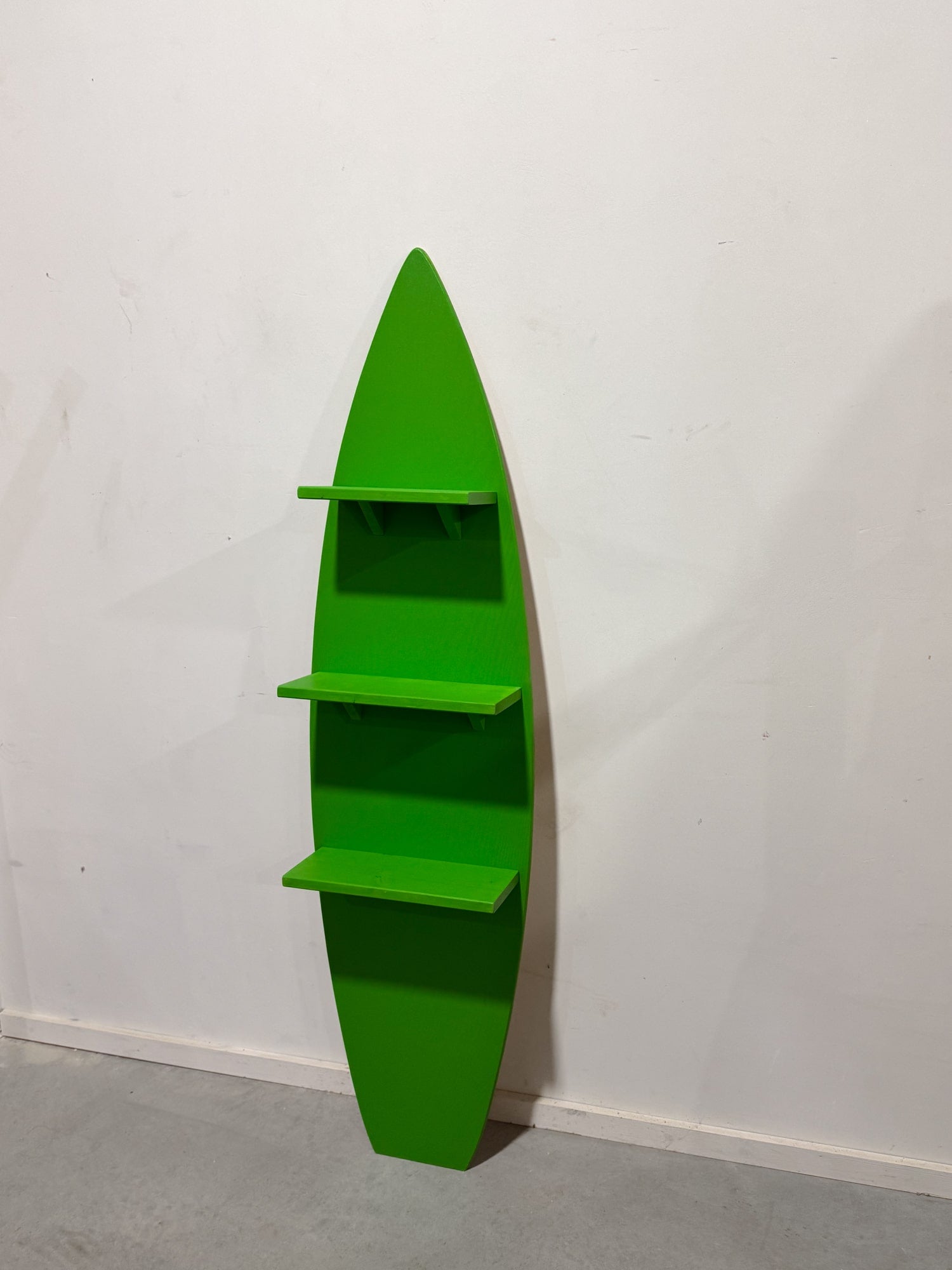 A unique green surfboard-shaped shelving unit with three spacious wooden shelves